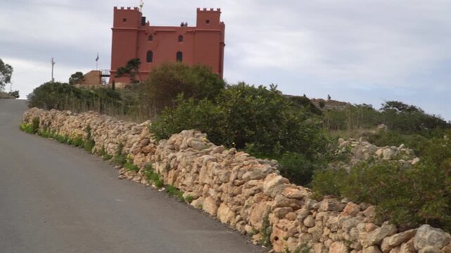 Local asphalt road leading towards the historic Red Tower (Saint Agatha's Tower) in Malta. Cloudy sky.