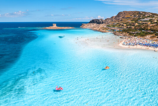 Aerial view of famous La Pelosa beach on sunny summer day. Stintino, Sardinia island, Italy. Top view of sandy beach, swimming people, clear blue sea, old tower and sky with clouds. Summer vacation
