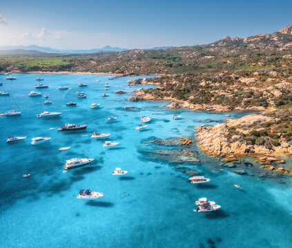 Aerial view of luxury yachts and boats on blue sea, beautiful island, mountain on summer sunny day. Sandy beach, rocky sea coast, azure transparent water in Sardinia, Italy. Top drone view. Seascape