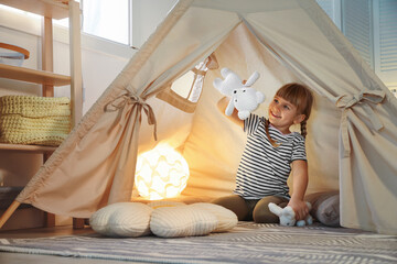 Little girl playing with toys in wigwam at home © New Africa