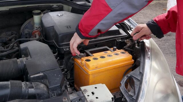 Mechanic replacing dead car battery under the hood, disconnecting terminals with wrench and removing the old accumulator for maintenance, repair service or recycling