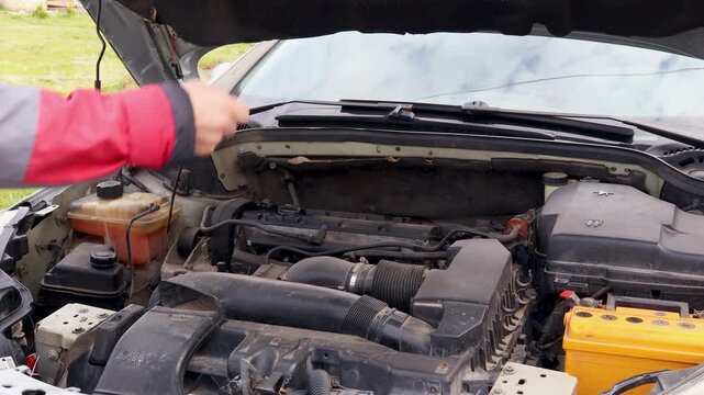 Professional mechanic performing car engine diagnostics and maintenance under the open hood, checking vehicle components and systems in an automotive service repair garage