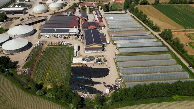 Aerial View of an Organic Farm: An expansive aerial view showcases a sustainable organic farm with solar panels, greenhouses, biogas digesters, and cultivated fields.