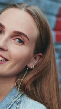 Vertical close up of Caucasian woman looking at camera. Female smiling with gentle expression. Urban street background. Woman posing for portrait while enjoying casual day outside.