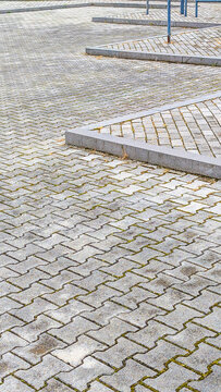 Interlocking paver blocks forming a durable, textured surface on an outdoor public square, creating a repetitive geometric pattern with concrete curbstones defining raised sections
