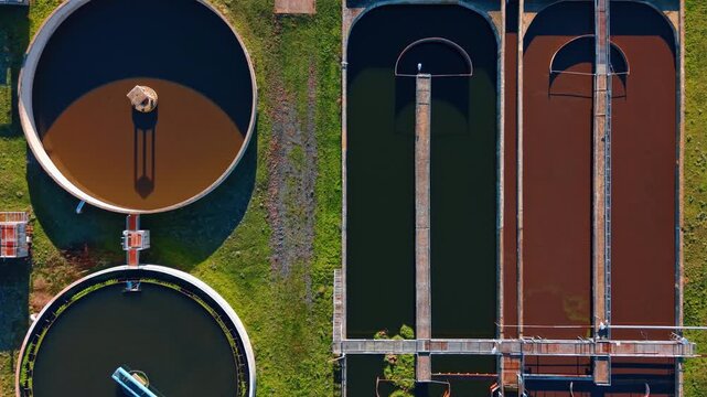 Industrial water treatment clarifiers and basins from above. Detailed top down view of circular sewage tanks and rectangular water purification systems with brown liquid.