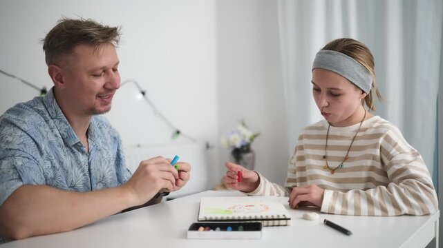 Father daughter unwrap colorful crayons at white table.