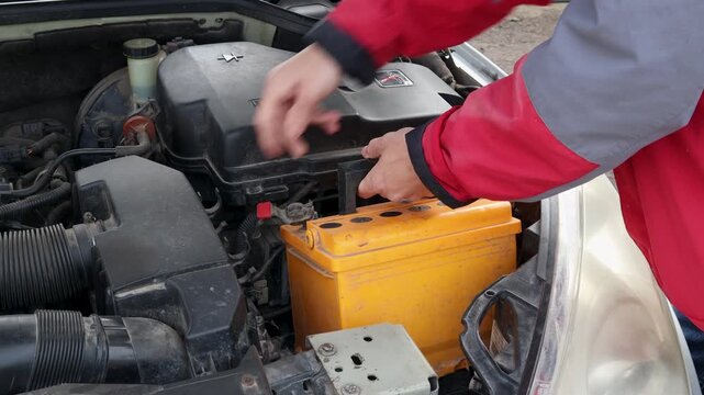 Mechanic installing new yellow car battery under hood, automotive maintenance service, vehicle engine repair, connecting positive and negative terminals, power supply