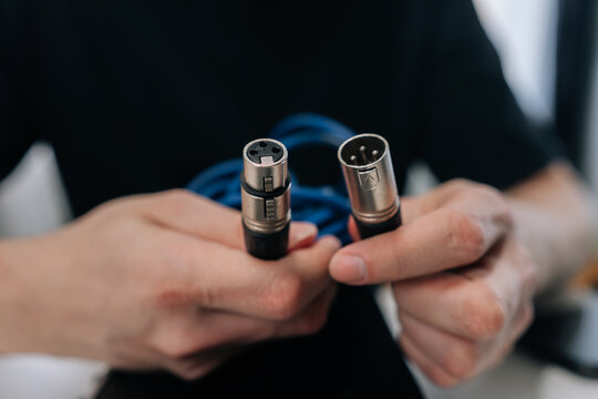 Musician hands holding male and female xlr cable connectors, preparing to connect them to audio interface for recording or live sound production in home studio.