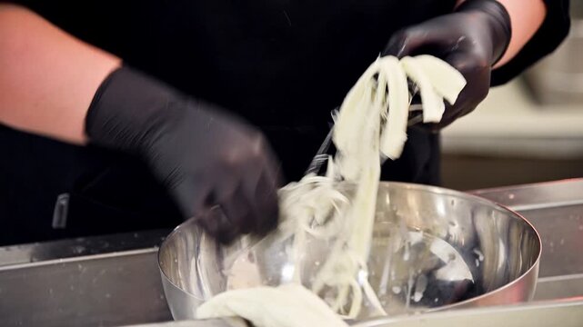 Chef prepares stracciatella cheese by stretching and shaping curds in a bowl