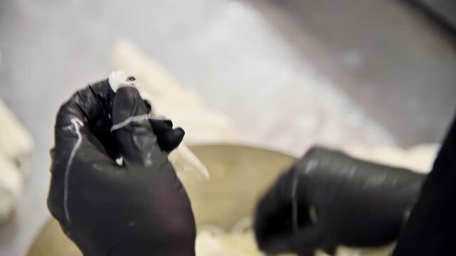 Hands preparing stracciatella cheese in a bowl, showcasing the stretching process