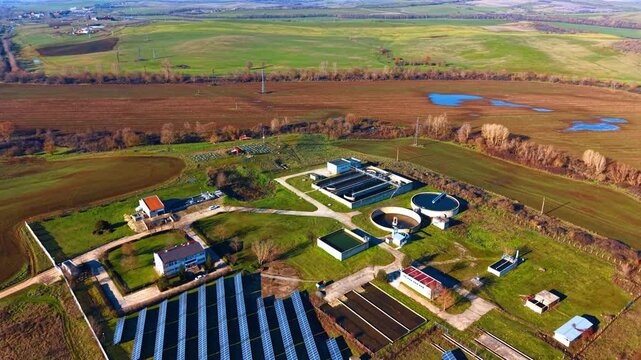 Wide aerial view of wastewater treatment facility and landscape. Panoramic drone shot of industrial water plant and solar farm surrounded by agricultural fields.