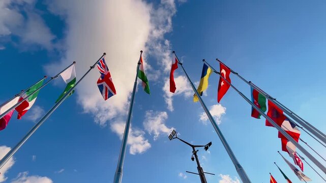 International national flags on tall flagpoles waving in strong wind against blue sky with clouds. Global unity, international relations, diplomacy and cooperation concept