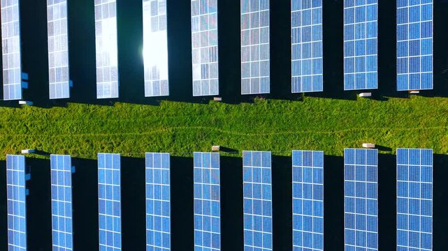 Symmetrical aerial shot of solar energy station. Top down view showing two blocks of photovoltaic panels separated by a green grass path.