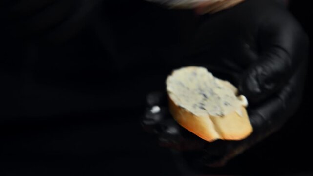 Chef spreads creamy cheese on bruschetta slice with a spoon in a dark kitchen