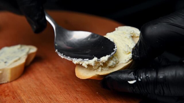 Preparing bruschetta with butter and cheese on wooden cutting board
