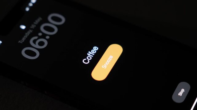 A smartphone alarm rings at 6 AM with the coffee label on a dark screen showing a snooze button in low light during an early morning wake up routine. High quality 4k footage