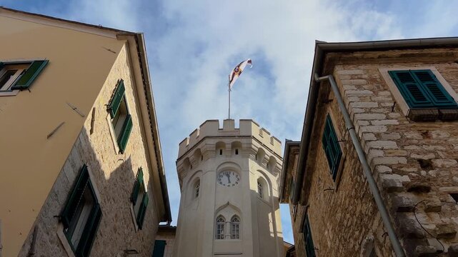 Historic clock tower with a flag with the city coat of arms between old stone houses in the old town of Herceg Novi, Montenegro. Architecture, city landmark and cultural heritage concept