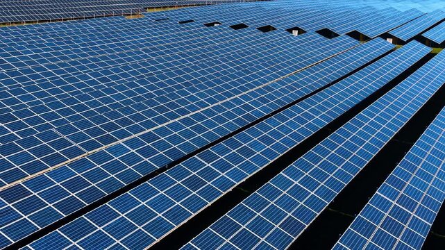 Perspective view of blue photovoltaic solar panels array. High angle aerial shot of rows of blue solar panels stretching across the rural frame.