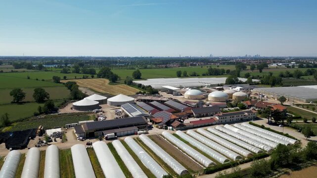 Renewable Energy Facility: An aerial view showcases a sprawling agricultural complex featuring solar panels, greenhouses, and anaerobic digesters, highlighting sustainable energy production.
