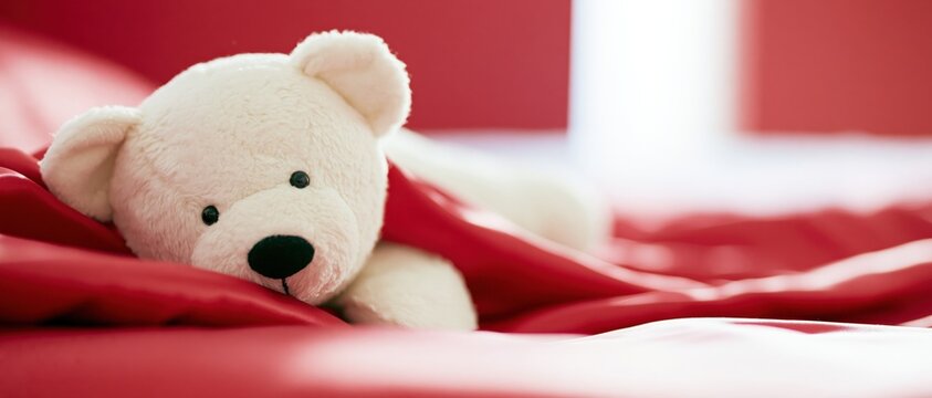 White teddy bear lying on red bed with soft linens