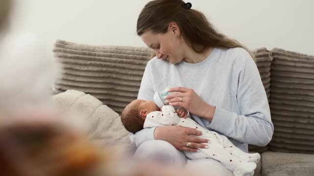 Mom Smiling Feeds Newborn From Bottle On Couch
