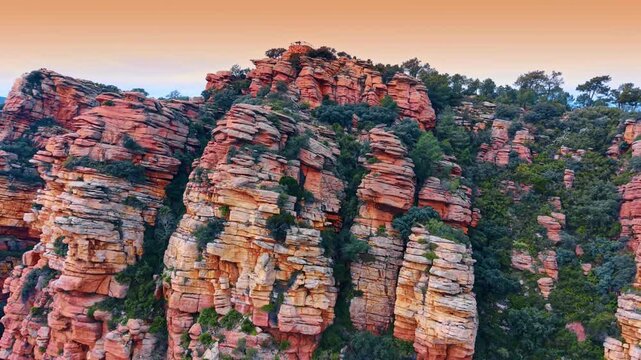 Eroded red sandstone pillars with layered texture at sunset light. Red sandstone with visible sedimentary layers and green plants under warm sky.