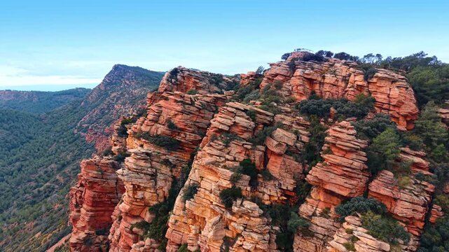 Red sandstone rock formation with layered geological structure and vegetation. Side view of eroded red sandstone pillars with horizontal layers under a clear blue sky in Spain.