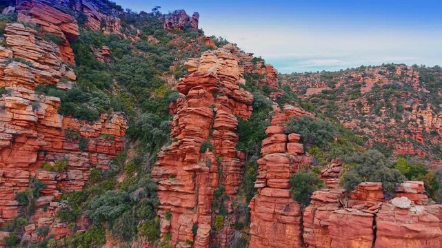 Red sandstone rock towers and ridges under blue sky. Wide view of several weathered red rock pillars and slopes covered in Mediterranean vegetation.