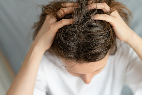 A woman gazes at her reflection with visible sadness over new gray hairs. The older adult feels disappointed by this mark of aging. Mother struggles with emotional weight of silver strands.