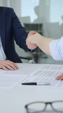 Business professionals shaking hands over a conference table with contract documents, symbolizing a successful partnership, agreement, deal, and collaboration in an office meeting