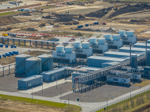 Aerial view of data center cooling infrastructure with cooling towers, water storage tanks, industrial piping systems, and utility buildings within a high-tech industrial complex.