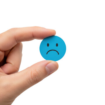 Fair-toned human hand holding a vibrant blue paper circle with a minimalist black drawn frowny face against a solid white studio background, ironic playful mood