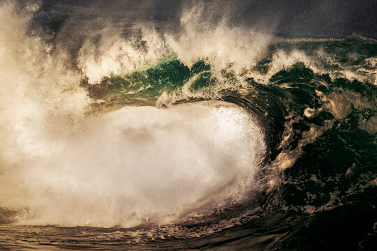 Large powerful ocean wave breaking over shallow reef in dramatic golden light along the New South Wales coastline, Australia.