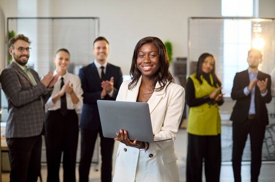 Businesswoman leader with laptop amid team applause. In a bright office the group applauds a corporate presenter, highlighting success and recognition. Strong leadership and teamwork concept.