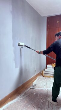 Professional painter renovating home interior with white paint roller and extension pole