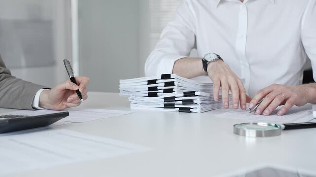 Professionals handling a large stack of documents and paperwork, signing a contract in a busy office. Audit and taxes in business