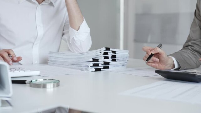 Professionals handling a large stack of documents and paperwork, signing a contract in a busy office. Audit and taxes in business