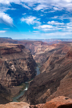 Sweeping canyon vista with layered red cliffs, deep river gorge, and vivid blue sky, capturing dramatic desert landscape beauty.