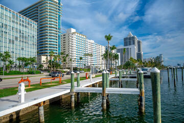 Obraz premium Miami, USA, 16 April 2026: Waterfront pier overlooking coastal city buildings and road in Miami. Wooden pier with white posts next to high rise buildings and a street in Miami Beach Florida.