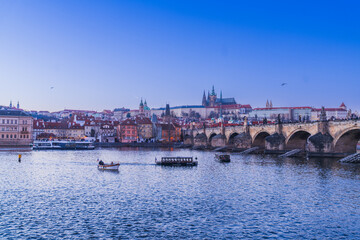 Fototapeta premium Panoramic twilight view of the historic Charles Bridge, Vltava River with tour boats, and Prague Castle on the hill, Prague, Czech Republic.