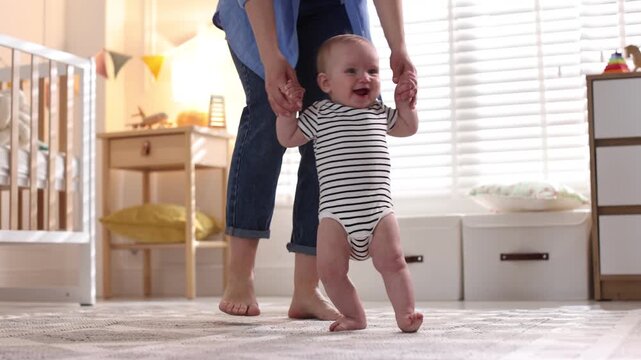 First steps. Mother supporting daughter while she learning to walk at home, closeup