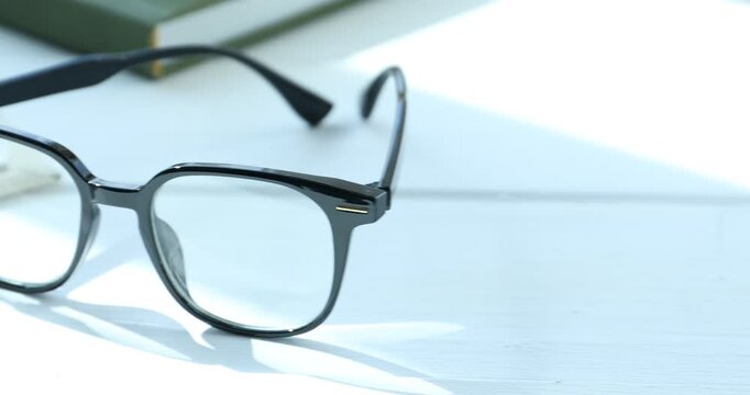 Stylish glasses and books on white wooden table indoors, closeup. Camera moving right
