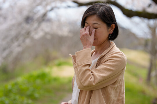 桜咲く公園で目を押さえるシニア女性