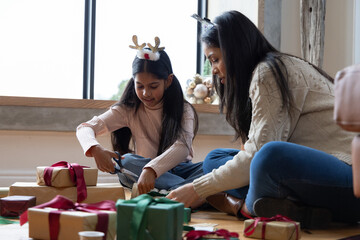 Indian mother and daughter wearing knit sweaters sitting at home wrapping kraft gifts with scissors © wavebreak3