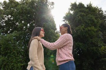 Two female friends standing facing each other in park wearing red-framed sunglasses and sweaters © wavebreak3