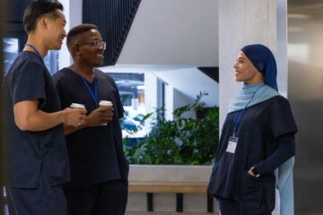 Naklejka premium Diverse medical coworkers standing and talking in clinic lobby wearing navy scrubs holding coffee