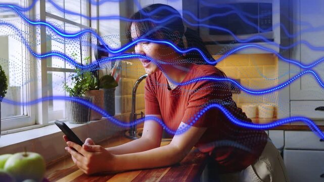Woman leaning on kitchen counter tapping phone, causing blue wave overlay while scrolling tech feed