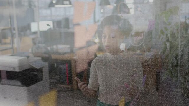 Woman standing behind writable glass, raising marker and gesturing while explaining business plan