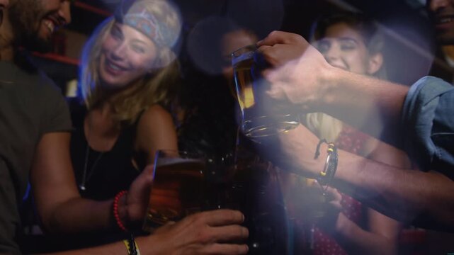 Friends clinking beer mugs as hands meet, cheering nightlife while camera zooming out showing bokeh